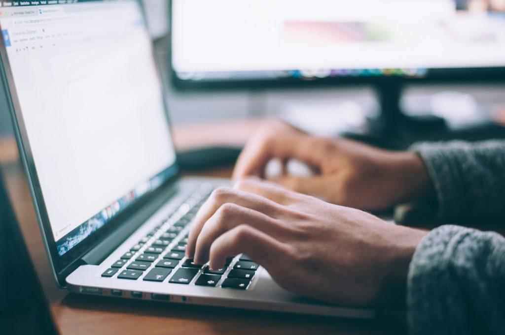 Hands typing on a laptop with a blurred screen in the background.