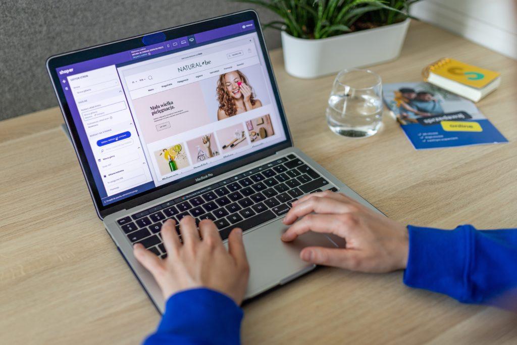 A laptop with an ecommerce business on the screen and two hands on the laptop.